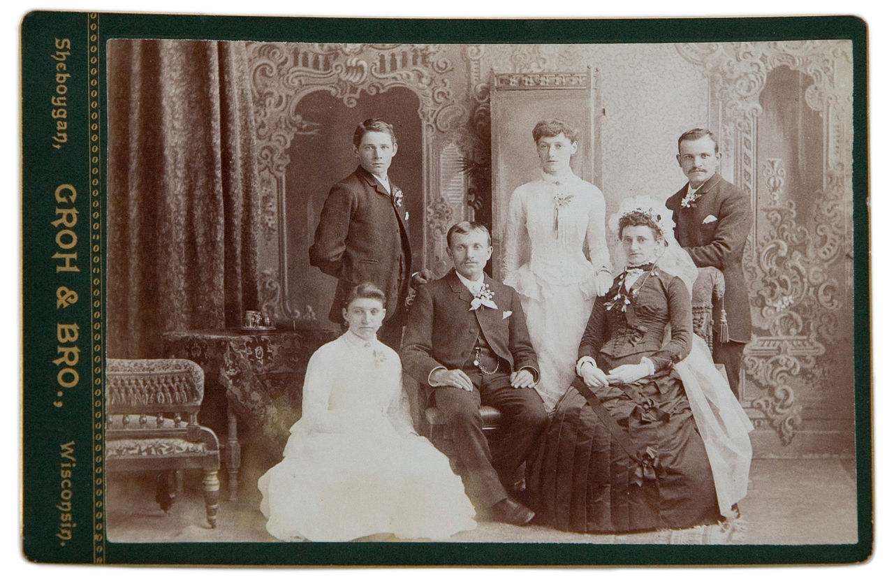 Late nineteenth-century studio cabinet card photograph of a family, showing clothing detail, jewelry, and the studio's embossed photographer mark on the card mount.