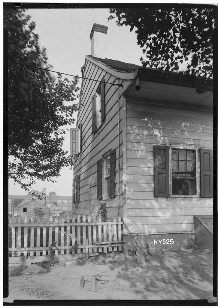 Large-format architectural photograph of a historic interior or porch detail, showing wood trim, wainscoting, door casing, and floor transitions at high resolution.